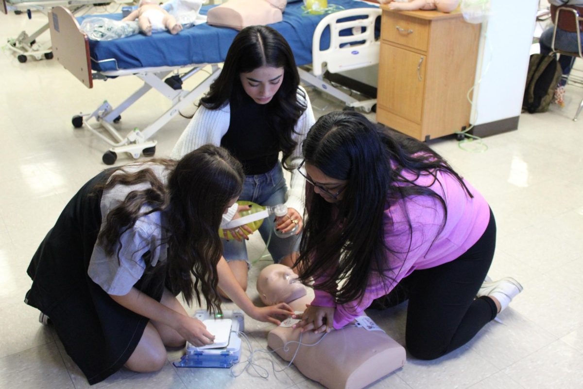 Seniors Giselle Aguilar, Litzy Topete, and Dania Garcia-Lucero perform CPR on a test dummy in the Foundations of Nursing class through ROP.  While students used to learn CPR in health classes, changes in the curriculum have made learning it more of a challenge.